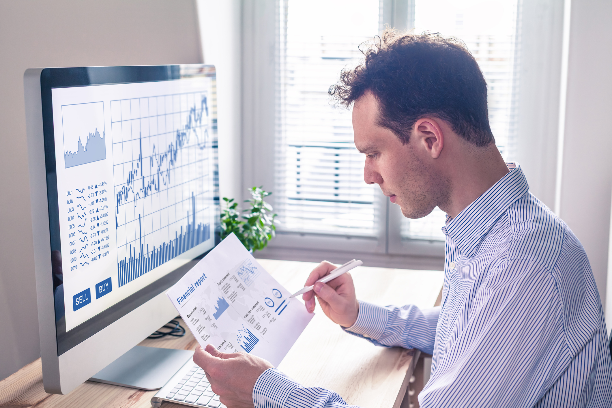 Male business worker in front of a computer monitor at desk holding a chart of financial numbers